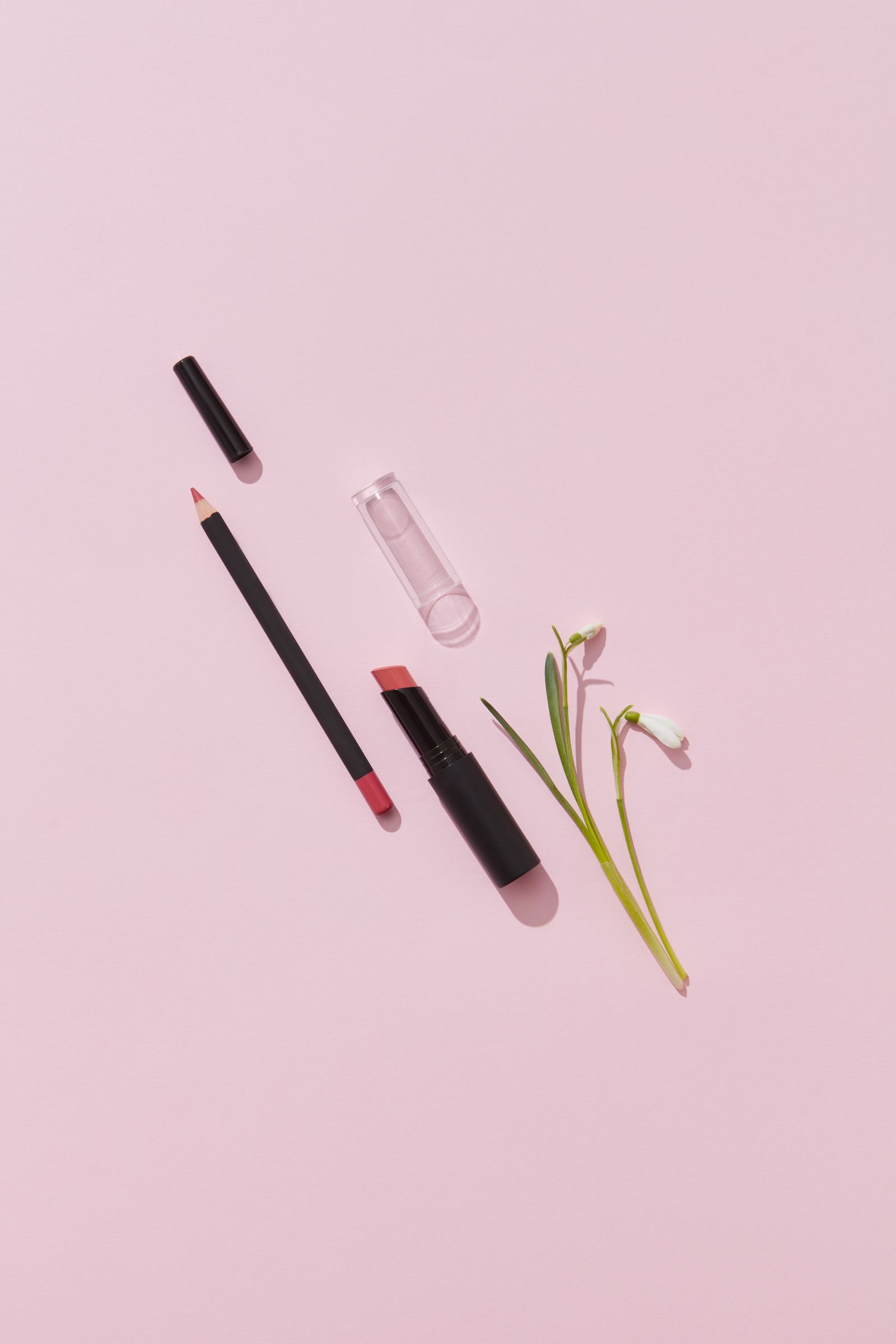 Lipstick and lip pencil with a flower on a soft pink background